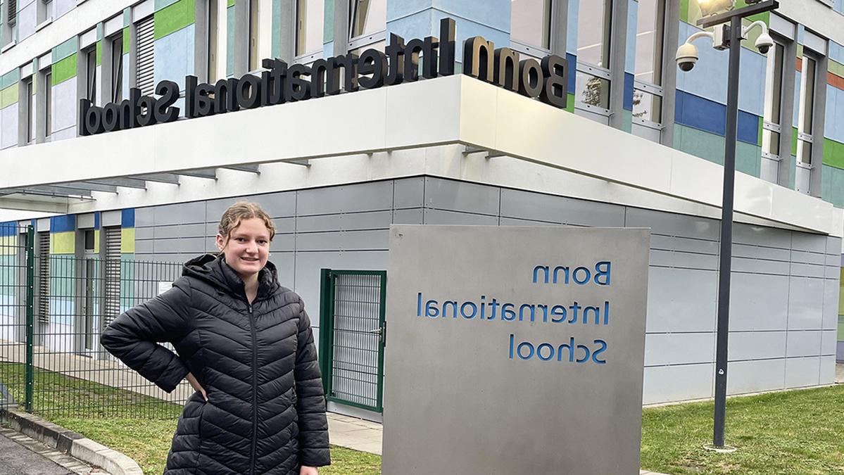 Woman standing in front of Bonn International School sign.